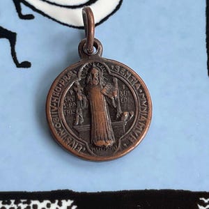 May include: A bronze Saint Christopher medal with a loop for hanging. The medal features a depiction of Saint Christopher carrying a child on his shoulder, with the inscription "S. CHRISTOPHORUS" around the edge.