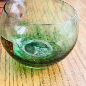 Puede incluir: Un vaso Mikasa claro y redondo con un interior verde. El vaso tiene un dise&ntilde;o &uacute;nico con una apariencia de burbuja. El vaso est&aacute; sobre una superficie de madera.