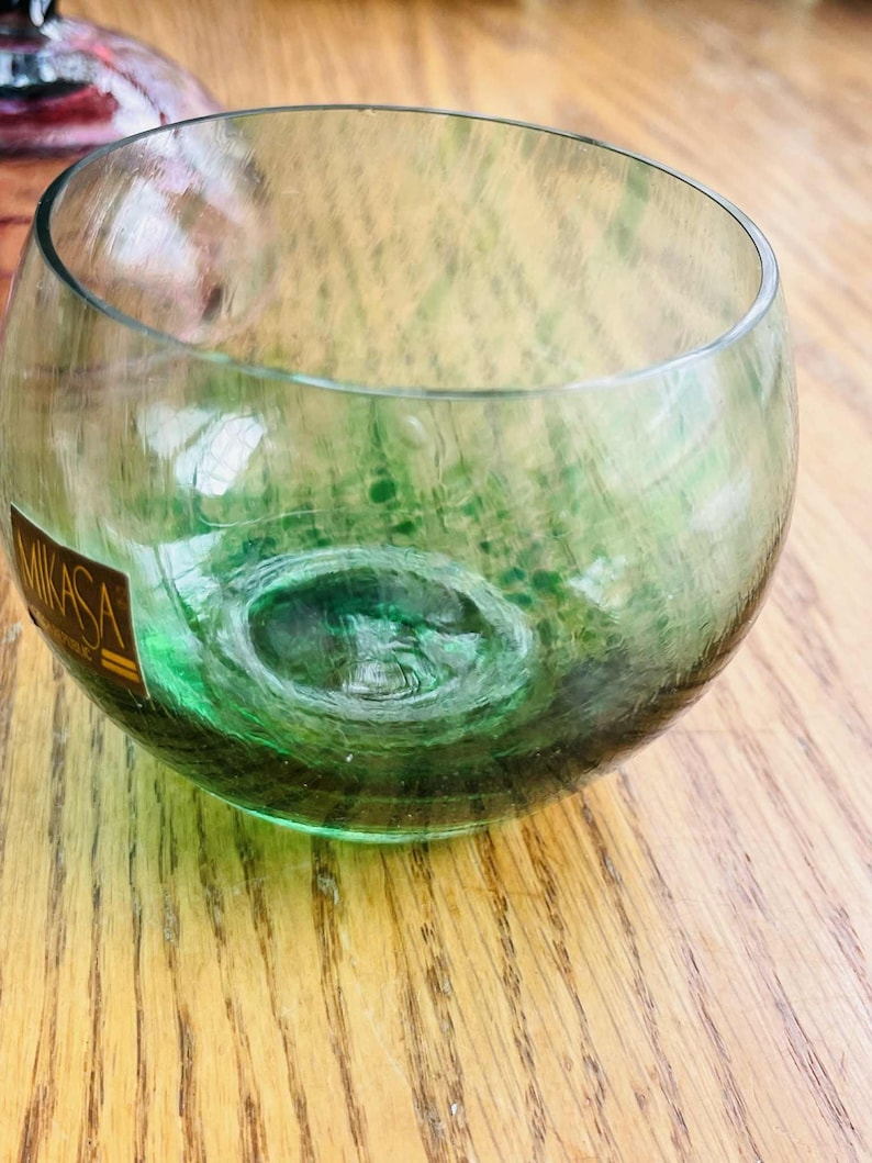 Puede incluir: Un vaso Mikasa claro y redondo con un interior verde. El vaso tiene un dise&ntilde;o &uacute;nico con una apariencia de burbuja. El vaso est&aacute; sobre una superficie de madera.