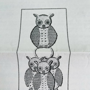 May include: Black and white crochet owl design with the text "Design 7298". The design features a large owl above three smaller owls, all connected by a metal ring. The owls have detailed feather patterns.