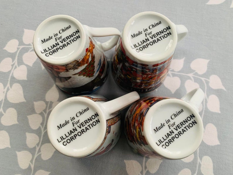 May include: Four white ceramic mugs with colorful designs and black text that reads "Made in China For Lillian Vernon Corporation" on the bottom of each mug.