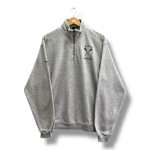May include: A grey sweatshirt with a quarter-zip collar and long sleeves. The front displays the text "BLAKE LACROSSE" with crossed lacrosse sticks in green. The left sleeve has the number "3" printed on it.