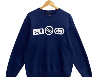 May include: A navy blue sweatshirt with the brand name "ecko" in white block letters and a rhino logo. The sweatshirt is displayed on a wooden hanger against a white background.