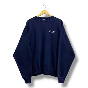 May include: A navy blue crew neck sweatshirt with the Motorola logo and "Radio Support Center" printed in white on the upper left chest. The sweatshirt is hanging on a wooden hanger against a white background.