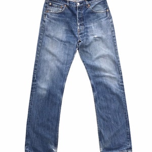 May include: A pair of blue denim jeans featuring a classic five-pocket design, a button fly closure, and a faded wash with whiskering details at the hips. The jeans have copper-colored rivets, contrast stitching, and a straight-leg silhouette.