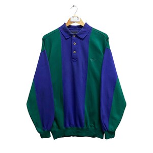 May include: A long-sleeve polo shirt featuring a color-blocked design in deep green and royal blue. The shirt has a classic collar, a three-button placket, and ribbed cuffs and hem. The fabric displays vertical panels of alternating colors.