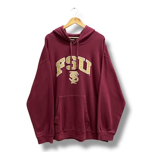 Può includere: Una felpa con cappuccio bordeaux con una tasca frontale e un cappuccio. La parte anteriore della felpa con cappuccio presenta il testo dorato "FSU" con un simbolo "$ " stilizzato. La felpa con cappuccio è appesa a una gruccia di legno.