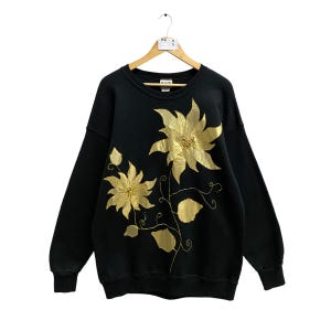 May include: Black sweatshirt featuring a gold embroidered floral design. The flowers are stylised and have a poinsettia-like shape.