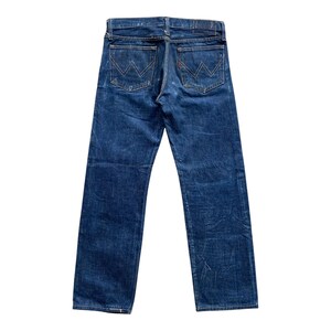 May include: A pair of dark blue denim jeans featuring a straight leg cut, a waistband with belt loops, and two back pockets. Each back pocket is detailed with a distinct white stitched W-shaped design and a small red tab on the right pocket.