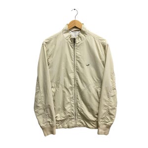 Op de afbeelding: Een beige ritsjack met een klein logo op de linkerborst.