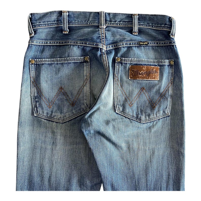 Pu&ograve; includere: Un paio di jeans blu denim con una toppa in pelle marrone Wrangler sulla tasca posteriore.