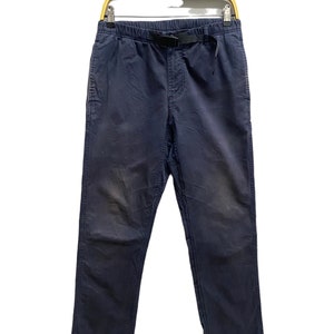 May include: Navy blue pants featuring an elastic waistband with an integrated black nylon webbing belt and a plastic buckle closure. The pants have a straight leg cut, side pockets, and visible stitching details along the seams and leg panels.