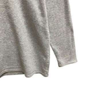 Puede incluir: Primer plano de una camiseta gris de manga larga. La camiseta est&aacute; hecha de una tela suave y texturizada. La manga es visible y el dobladillo tiene una abertura lateral. La camiseta es de color liso y parece de estilo casual.