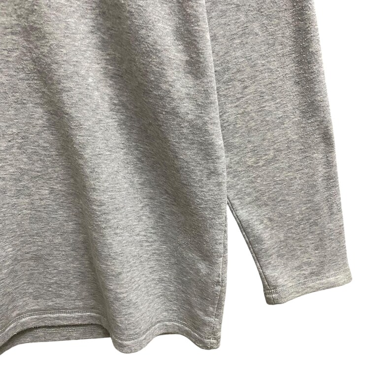 Puede incluir: Primer plano de una camiseta gris de manga larga. La camiseta est&aacute; hecha de una tela suave y texturizada. La manga es visible y el dobladillo tiene una abertura lateral. La camiseta es de color liso y parece de estilo casual.