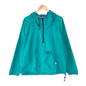 Op de afbeelding: Een turquoise blauwe hooded pullover jas met een ritssluiting en een kangoeroezak. De jas heeft een klein logo-patch op de zak met de tekst "Purveyor".