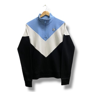 May include: A color-blocked sweatshirt with a light blue, white, and black design. The top features a high collar with a quarter-zip closure and the brand logo on the chest. The bottom hem and cuffs are ribbed.