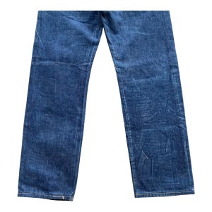 May include: A pair of dark blue denim jeans featuring a straight-leg cut with visible fading and whiskering patterns throughout the fabric. The denim has a textured appearance with subtle creasing and a classic stitched hem at the bottom of each leg.