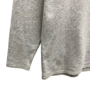 Puede incluir: Primer plano de una camiseta de manga larga gris jaspeado. La tela tiene un aspecto texturizado. La manga y el dobladillo son visibles, con una costura. La camiseta parece estar hecha de un material suave y c&oacute;modo.