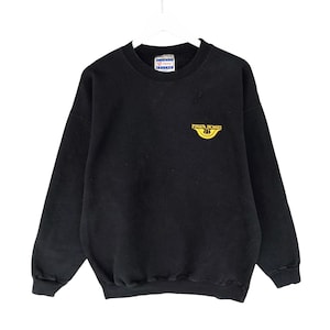 Puede incluir: Sudadera negra de cuello redondo con el texto "FUJITA HOMES" en amarillo. La sudadera está colgada de una percha blanca. La etiqueta de la marca es visible en la parte superior.