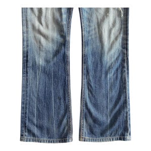 Pu&ograve; includere: Un paio di jeans blu denim con uno stile a zampa di elefante. I jeans hanno un aspetto sbiadito e sono consumati con alcuni buchi.