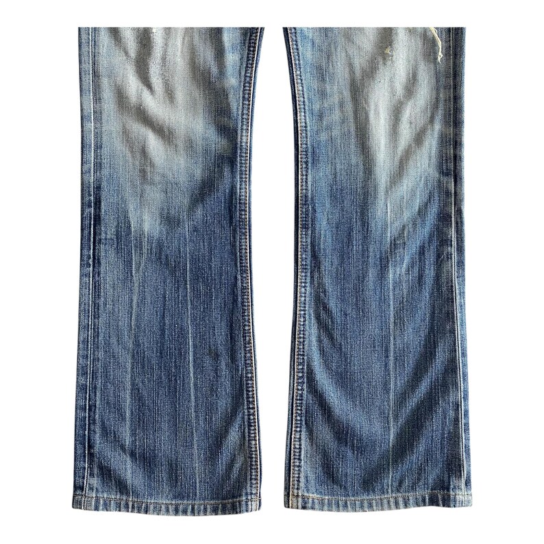 Pu&ograve; includere: Un paio di jeans blu denim con uno stile a zampa di elefante. I jeans hanno un aspetto sbiadito e sono consumati con alcuni buchi.