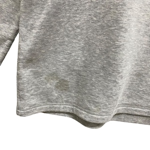 Puede incluir: Una camiseta de manga larga gris jaspeado con cuello redondo. La prenda tiene una mancha en la parte inferior delantera. La tela parece ser un material de punto suave.