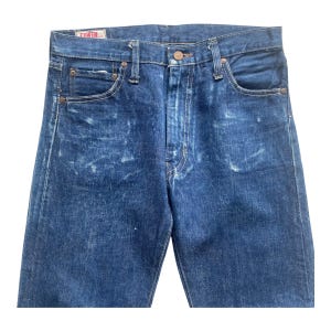 May include: Dark blue denim jeans featuring a faded wash pattern, a button fly closure, and five pockets. The waistband includes belt loops and a small white label with red text reading EDWIN stitched on the interior back of the waistband.