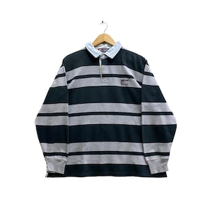 Könnte beinhalten: Ein langärmeliges Rugby-Shirt mit horizontalen Streifen in Dunkelgrün und Grau. Das Shirt hat einen hellblauen Kragen und einen kleinen Logoaufnäher. Der Markenname "CHAPS" ist auf dem Kragen sichtbar.