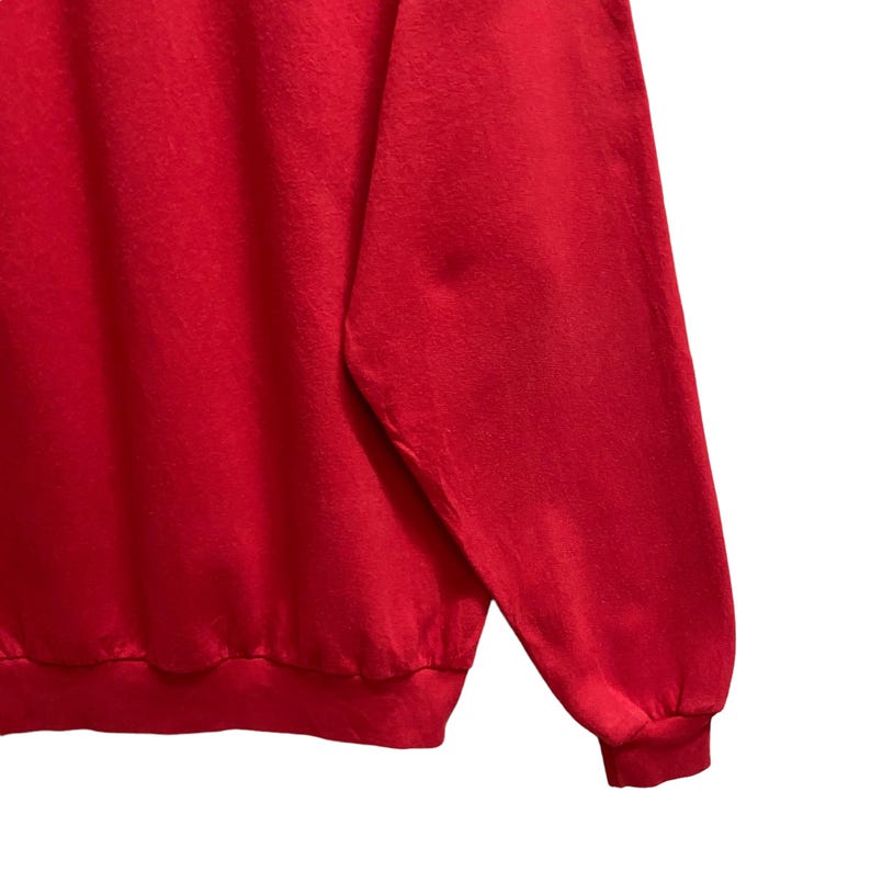May include: A close-up of a red sweatshirt sleeve. The sleeve is made of a soft, textured material. The cuff is ribbed and the bottom hem is also ribbed. The background is white.