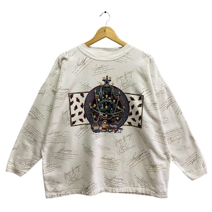 Puede incluir: Sudadera de manga larga de color crema con un diseño festivo de árbol de Navidad. El diseño presenta un árbol decorado con adornos y regalos, enmarcado por un borde rectangular con detalles en marrón. La camisa está cubierta con un patrón de escritura repetido.