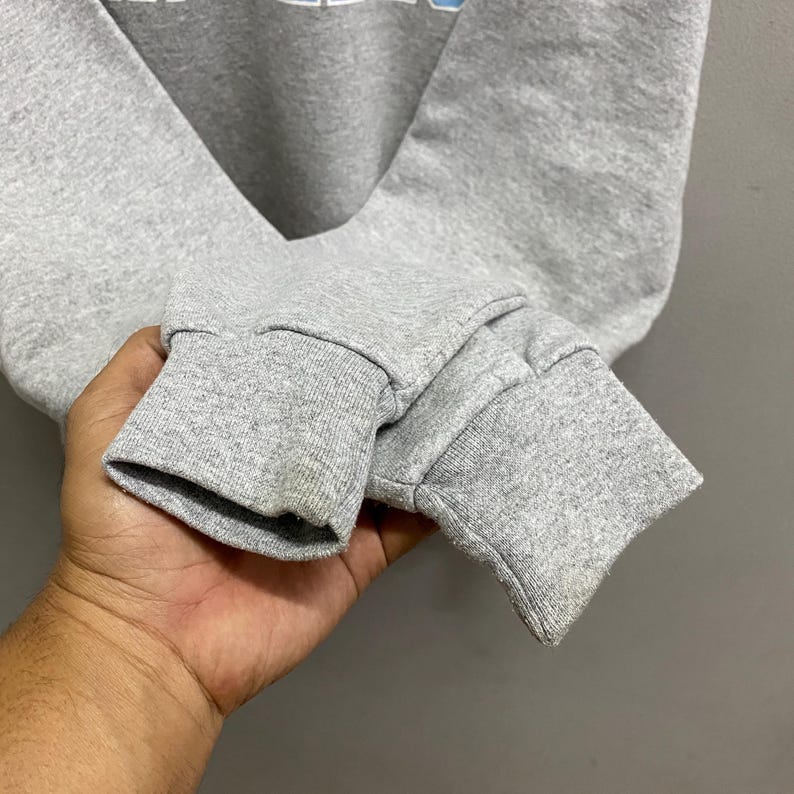 May include: Close-up of a gray sweatshirt sleeve with a ribbed cuff. The fabric appears to be a soft, medium-weight material. The cuff shows some discoloration.