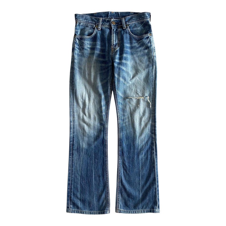 Pu&ograve; includere: Un paio di jeans blu denim con un aspetto consumato. I jeans hanno uno stile a zampa di elefante e sono realizzati in un tessuto morbido e confortevole.