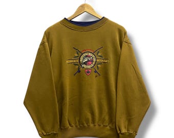 May include: Mustard-colored sweatshirt with a navy blue collar and cuffs. The front features an embroidered design with the text "Authentic Outdoors" and a graphic of a fish, crossed arrows, and a Canadian flag.