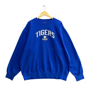 May include: A royal blue sweatshirt with the word "TIGERS" arched across the chest in white block letters. Below the word "TIGERS" is the text "ROTHSAY" and a tiger logo. The sweatshirt is hanging on a wooden hanger.