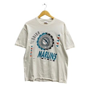 May include: White t-shirt featuring a graphic print of a marlin fish and the text "Florida Marlins".