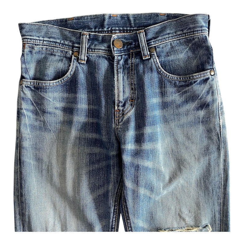 Pu&ograve; includere: Un paio di jeans blu in denim con dettagli sbiaditi e consumati. I jeans hanno uno stile classico a cinque tasche e una chiusura con bottone.