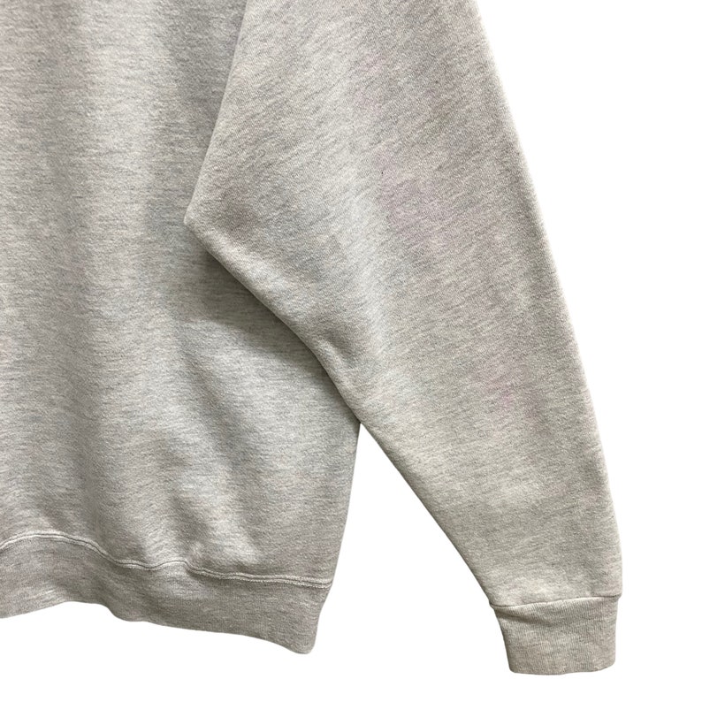 May include: A light gray sweatshirt with a crew neck and long sleeves. The cuff of the sleeve is ribbed. The fabric has a heathered texture.