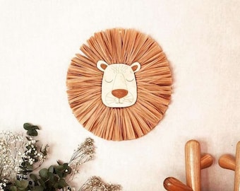 May include: A woven straw lion head wall decor with a white background and brown eyes. A stuffed lion toy is in a wicker basket with a peach colored blanket. A wooden stool with a white top has a stack of orange and gray blankets.
