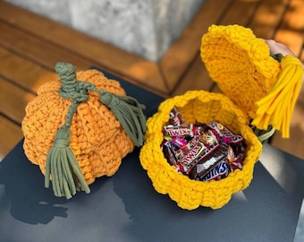 May include: Two crocheted pumpkin-shaped baskets, one orange and one yellow. The yellow basket is open and filled with chocolate candy bars. Both baskets have green tassels.