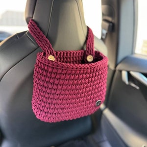 May include: A burgundy crocheted hanging organizer with two wooden buttons, hanging from the headrest of a car seat.