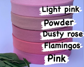 May include: Five spools of pink elastic fabric, stacked on top of each other. The spools are labeled from top to bottom: Light pink, Powder, Dusty rose, Flamingos, Pink.