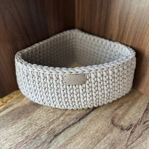 May include: A beige crocheted storage basket with a small silver tag that says "Aminika".