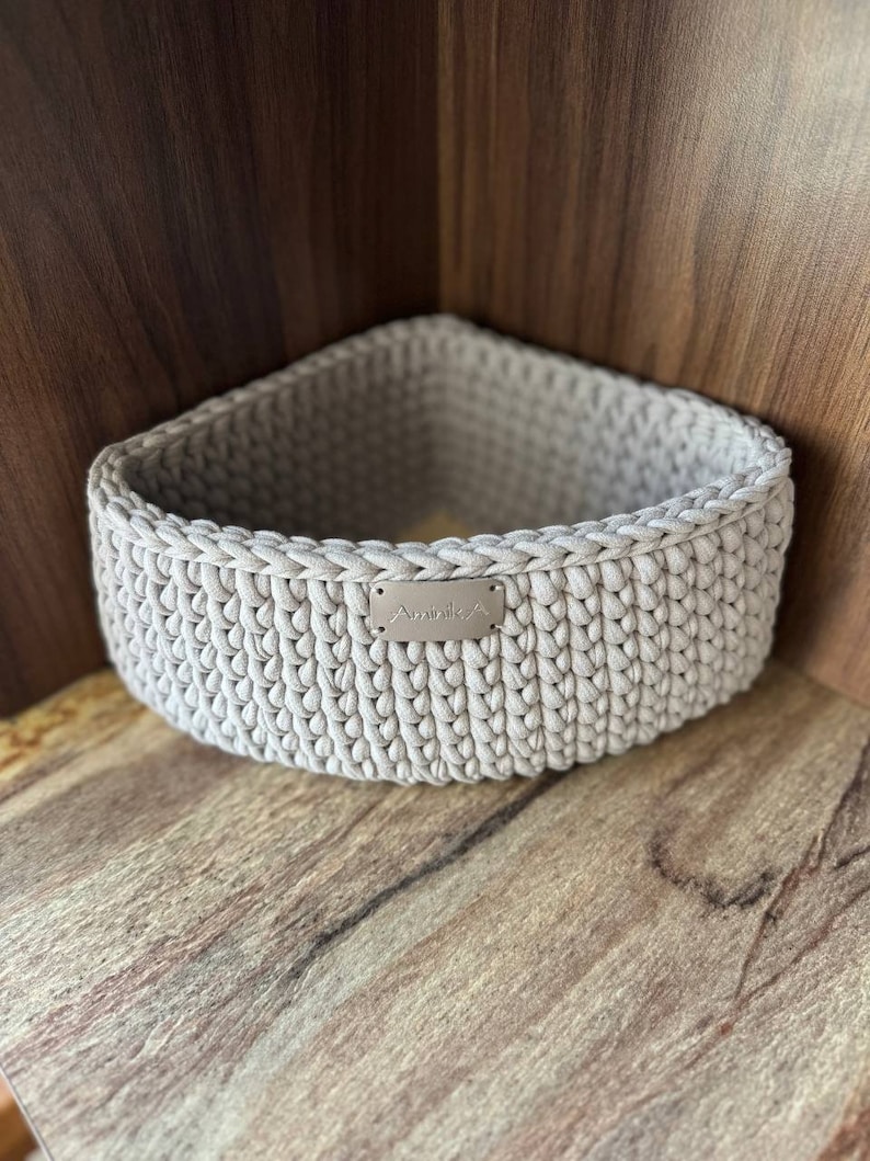 May include: A beige crocheted storage basket with a small silver tag that says "Aminika".