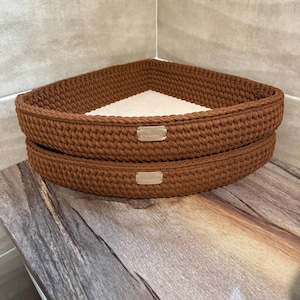 Può includere: Due mensole ad angolo in crochet marrone con una fodera in tessuto bianco. Le mensole sono impilate l'una sull'altra.