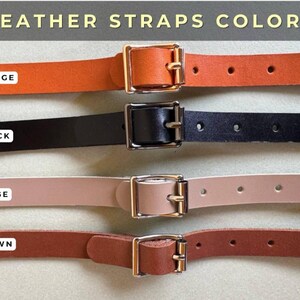 May include: Four leather straps in different colors: orange, black, beige, and brown. Each strap has a gold metal buckle and is shown against a light beige background.