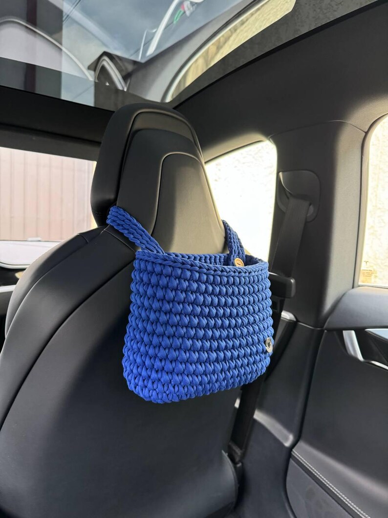 May include: A blue crocheted bag hanging from the headrest of a car seat.