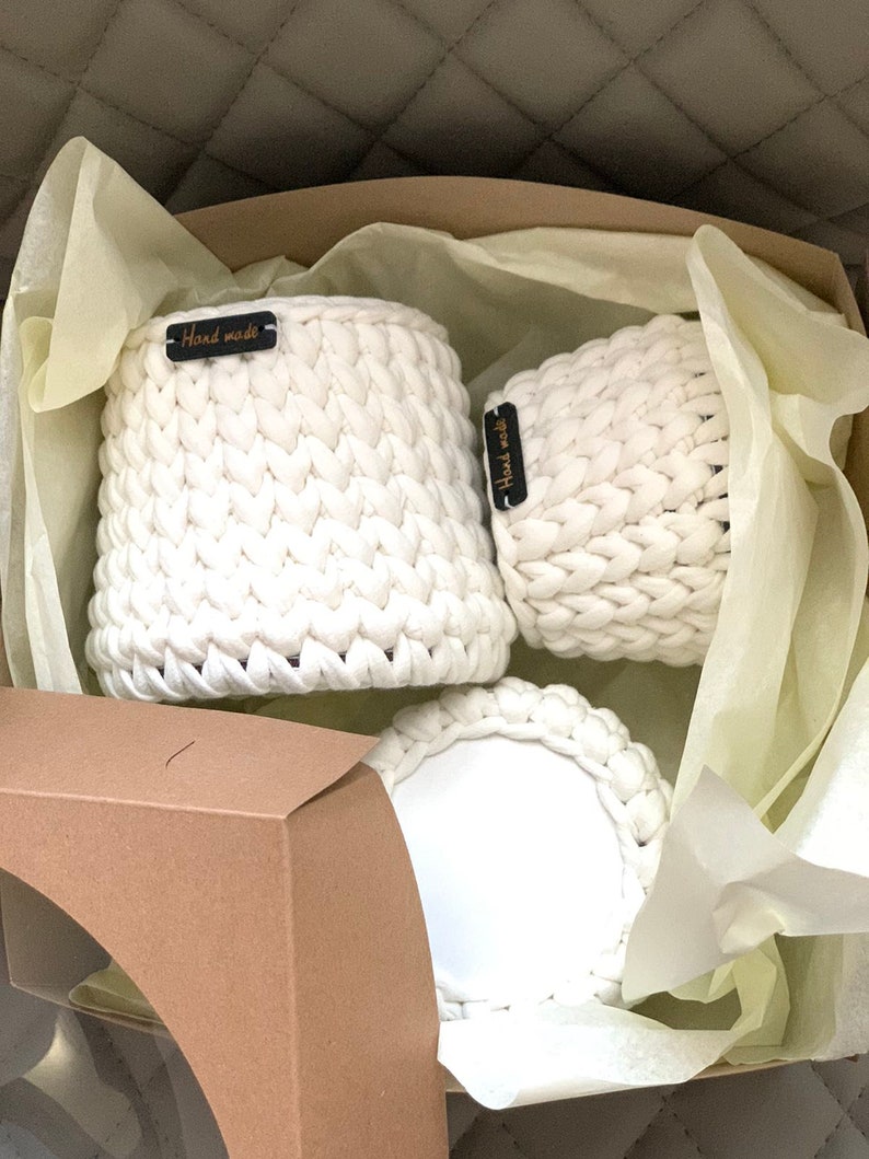 May include: Three white crocheted baskets with black labels that say "Handmade" in a brown box with white tissue paper.
