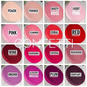 May include: A collection of 16 spools of colourful elastic ribbon, each with a different colour name printed on the spool. The colours include peach, powder, dusty rose, light pink, pink, flamingo, coral, red, wine, raspberry, fuchsia, rosewood, orchid, blueberry mousse, plum, and eggplant.