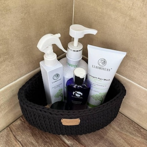 Könnte beinhalten: Ein schwarzer gehäkelter Korb mit vier Flaschen Haarpflegeprodukten. Die Flaschen sind mit "Shampoo", "Silk & Smooth", "Cleansing Complex" und "Collagen Hair Mask" beschriftet.