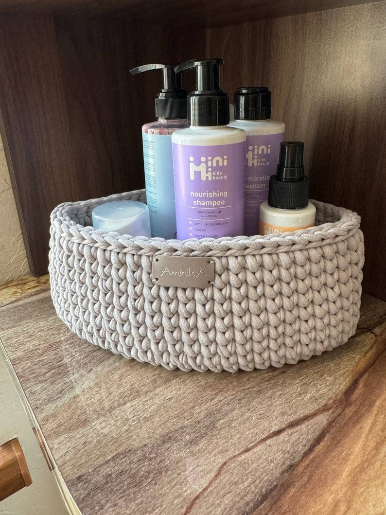 May include: A light gray crocheted basket with a silver label that says "Aminila" is filled with various bottles of kids beauty products. The bottles are labeled "mini kids beauty" and include a nourishing shampoo, micellar cleanser, and a spray bottle.
